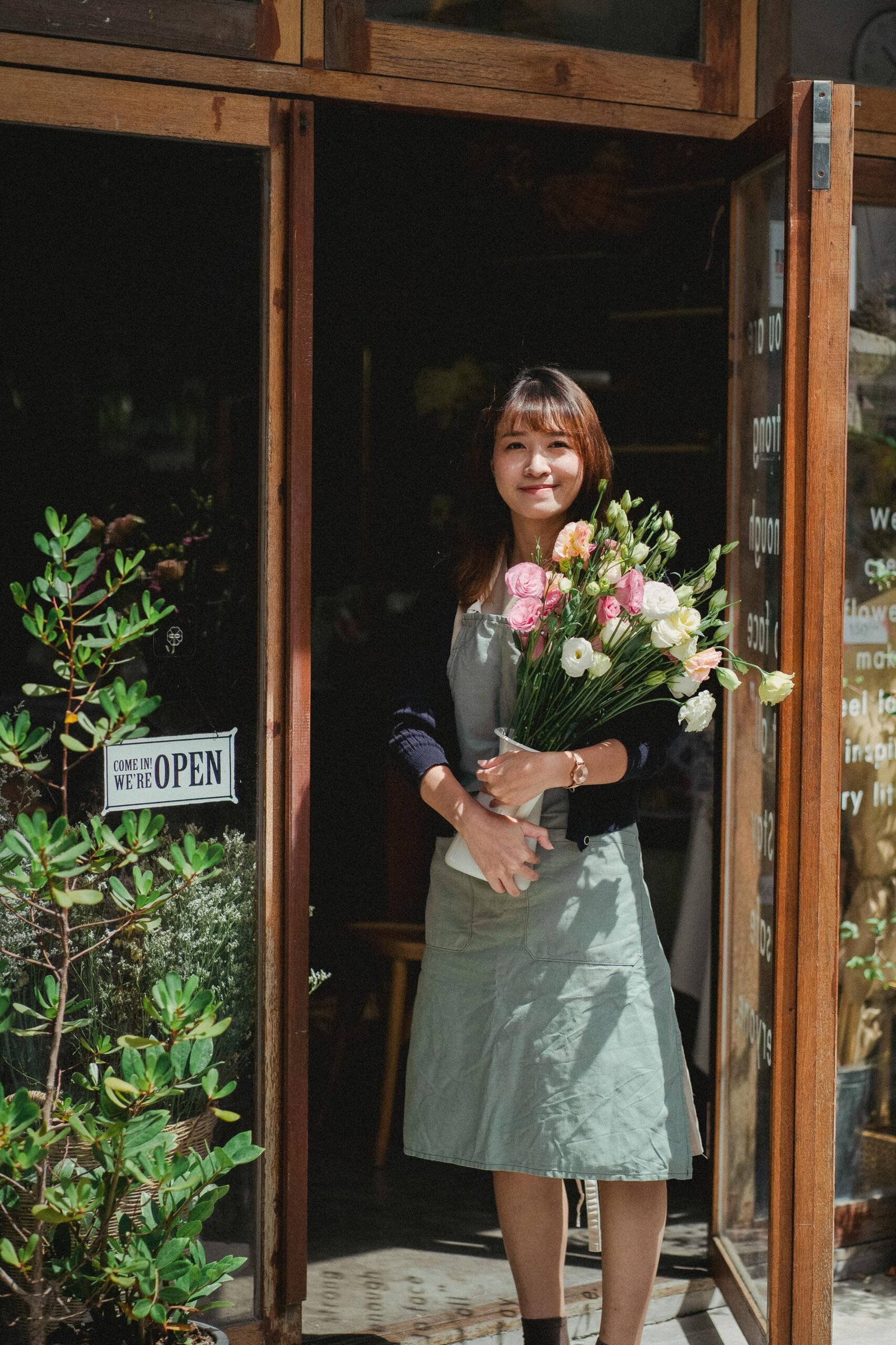 mujer sosteniendo un ramo de flores en la entrada de una florería